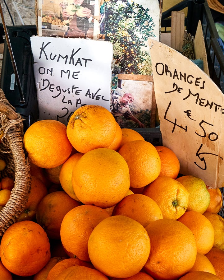 A vibrant display of fresh oranges in a market stall, accompanied by handwritten signs advertising 