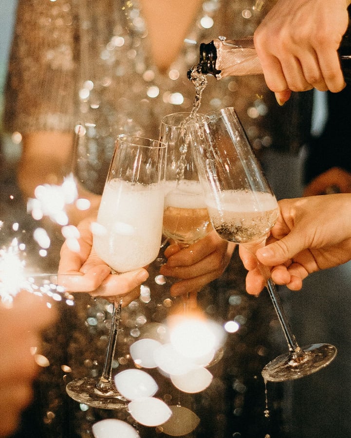 A celebratory moment captured with champagne being poured into flutes, sparklers glowing, and shimmering attire reflecting the festive atmosphere.