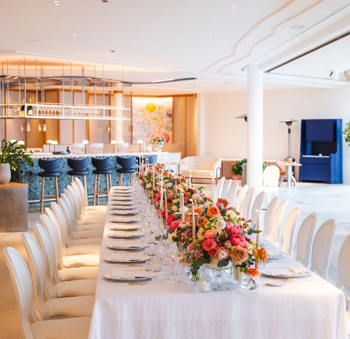 Longue table dressée d'une nappe blanche, de fleurs et de bougies devant un bar - Long table set up with a white tablecloth, flowers and candles in front of a bar