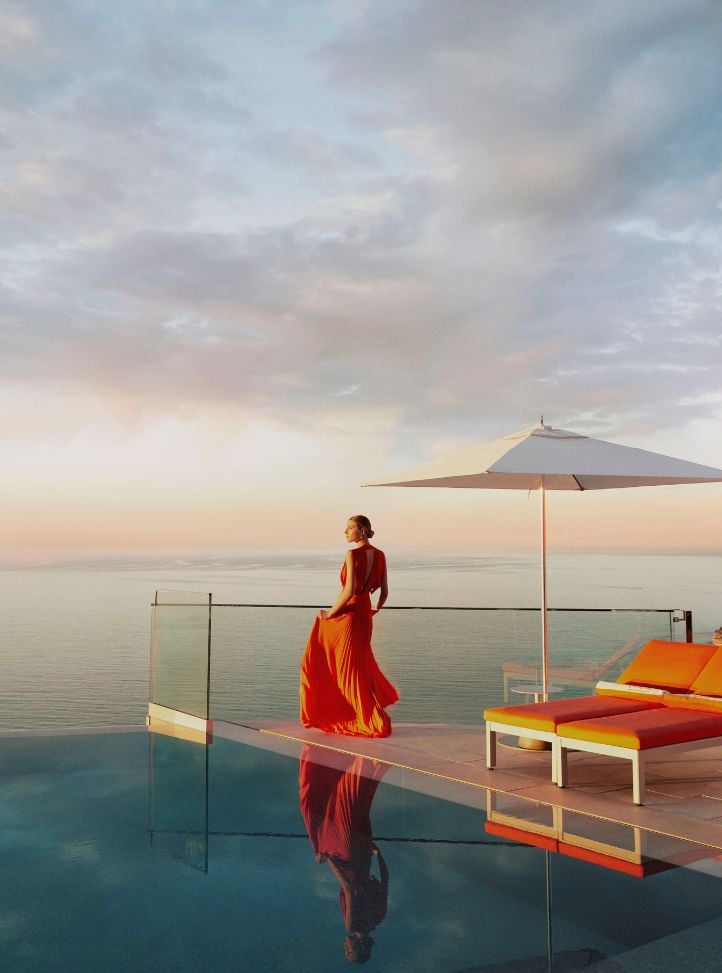 Femme en robe orange à côté d'une piscine à débordement face à la mer - Woman in an orange dress near the infinity pool with sea view