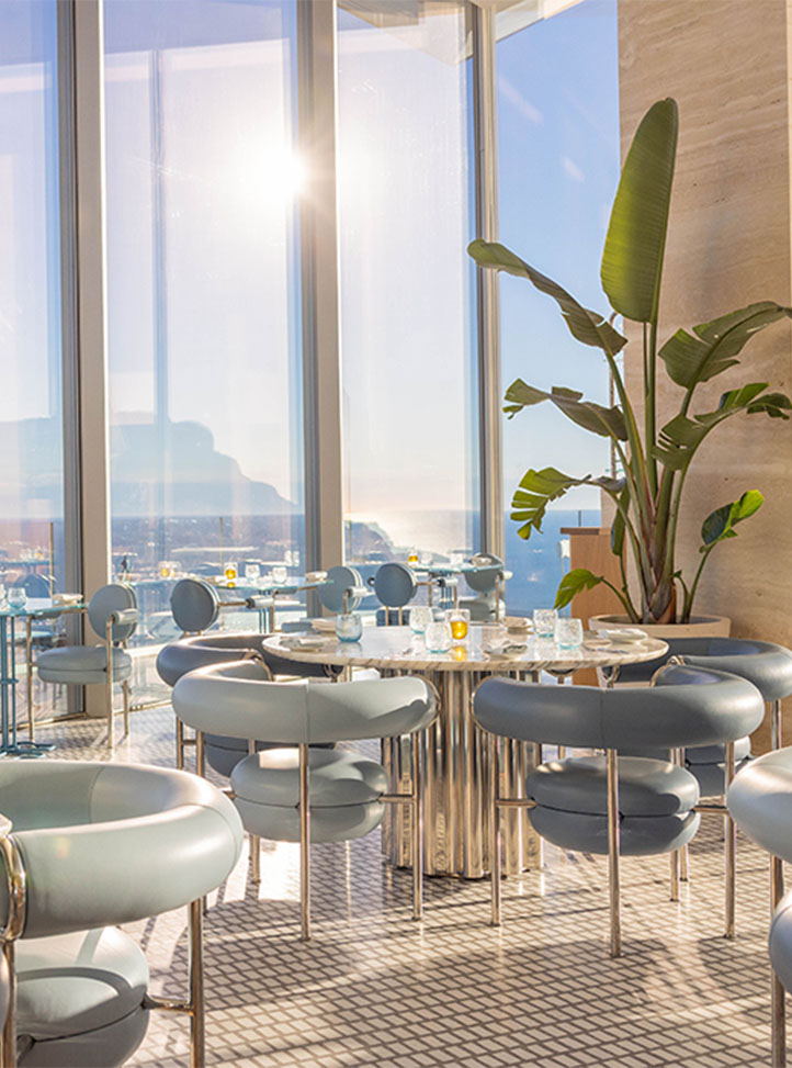 A serene and elegant dining room featuring modern furnishings, neutral tones, and expansive floor-to-ceiling windows that frame breathtaking ocean views.