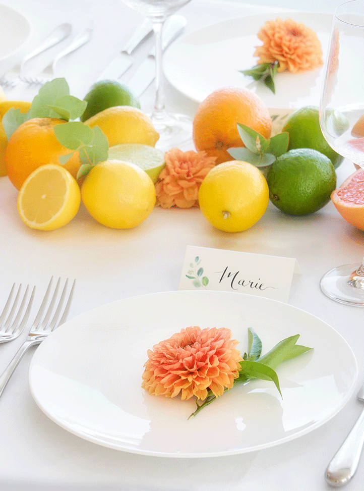 Beautiful place setting with orange dahlias, lemons and limes and a place name card with 'Marie' written in calligraphy.