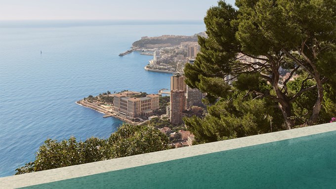 A panoramic view of a coastal city with tall buildings by the sea, seen from behind an infinity pool and framed by trees.