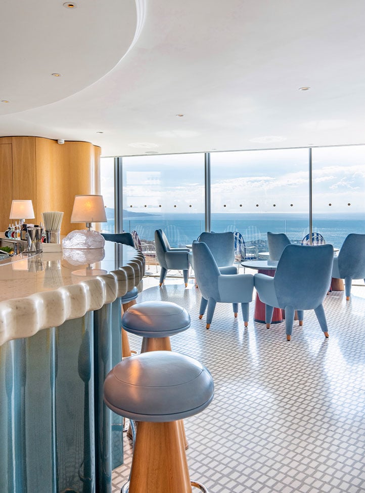 Bar 300, with bar on the left, table and chairs on the right and floor to ceiling windows with far reaching views of the tea. Blue and white tones.