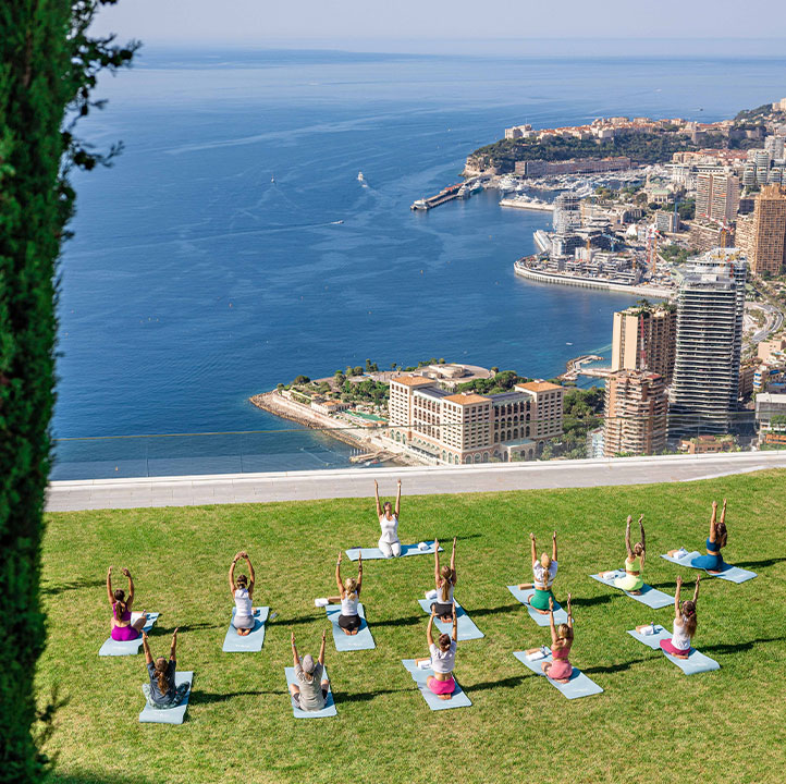 View of yoga glass taking place outside on the grounds of the hotel, overlooking Monaco and the sea.