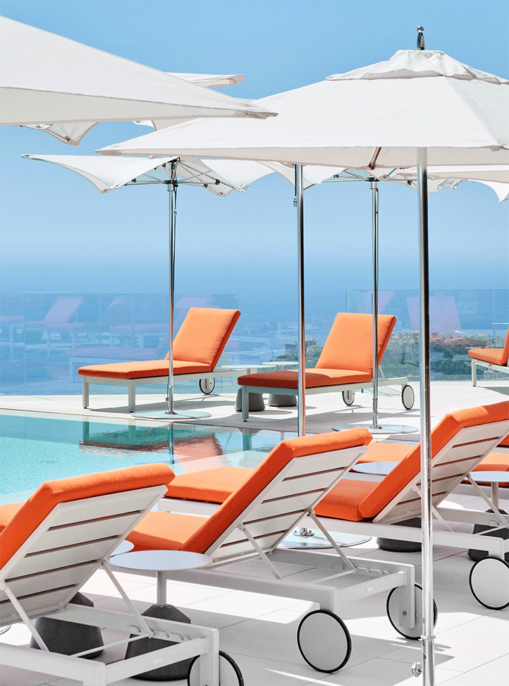 Orange sunbeds and white parasols by the pool, with a view of the sea in the background.